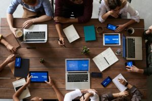 B2B marketing team collaborating during a strategy meeting with laptops and digital devices on a wooden table.