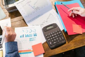 Two professionals analysing financial and marketing performance charts with a calculator and reports on a wooden desk.