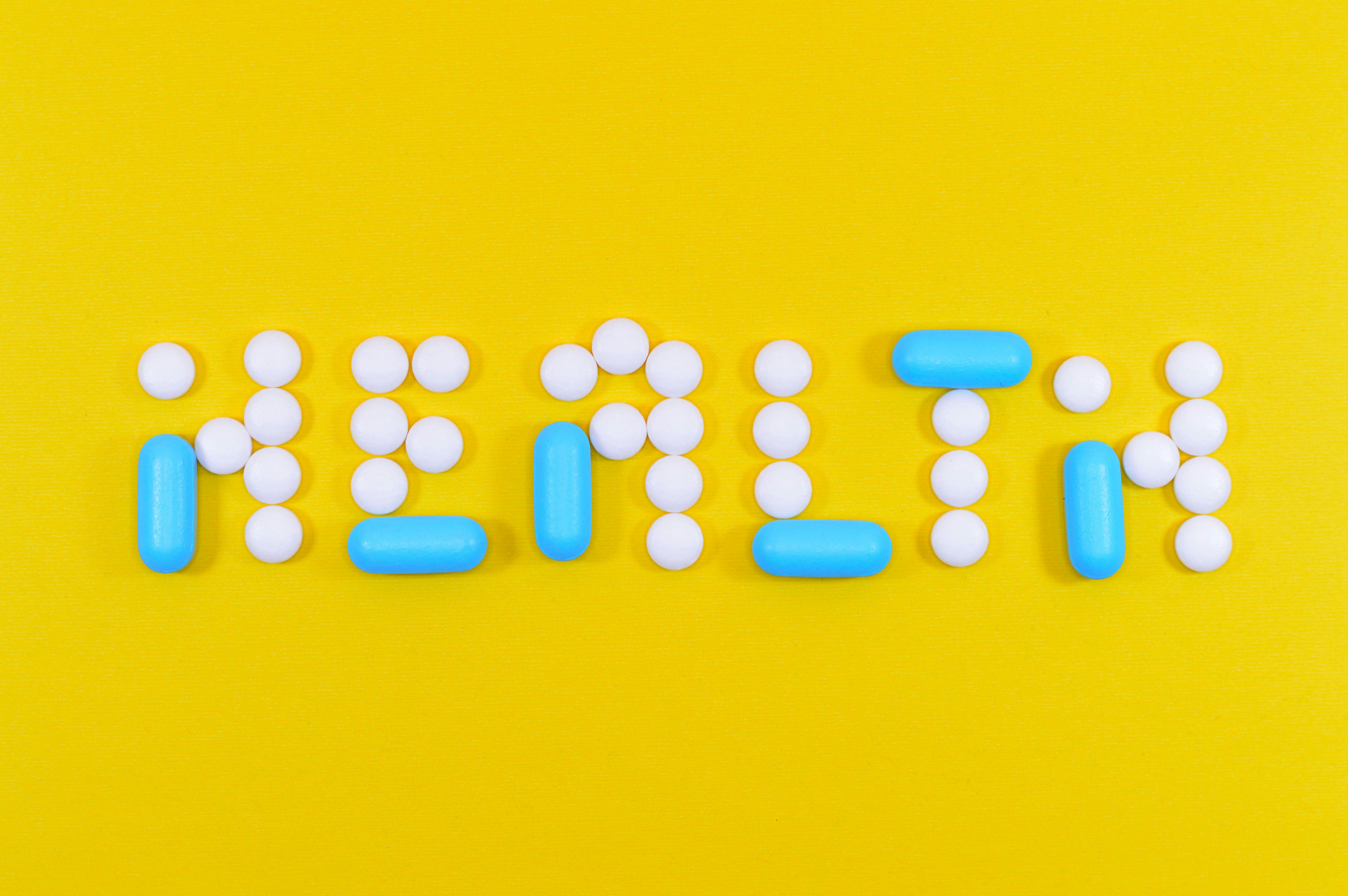 White and blue pills arranged to spell ‘HEALTH’ on a bright yellow background, representing healthcare marketing in pharma, medtech, and medical services.