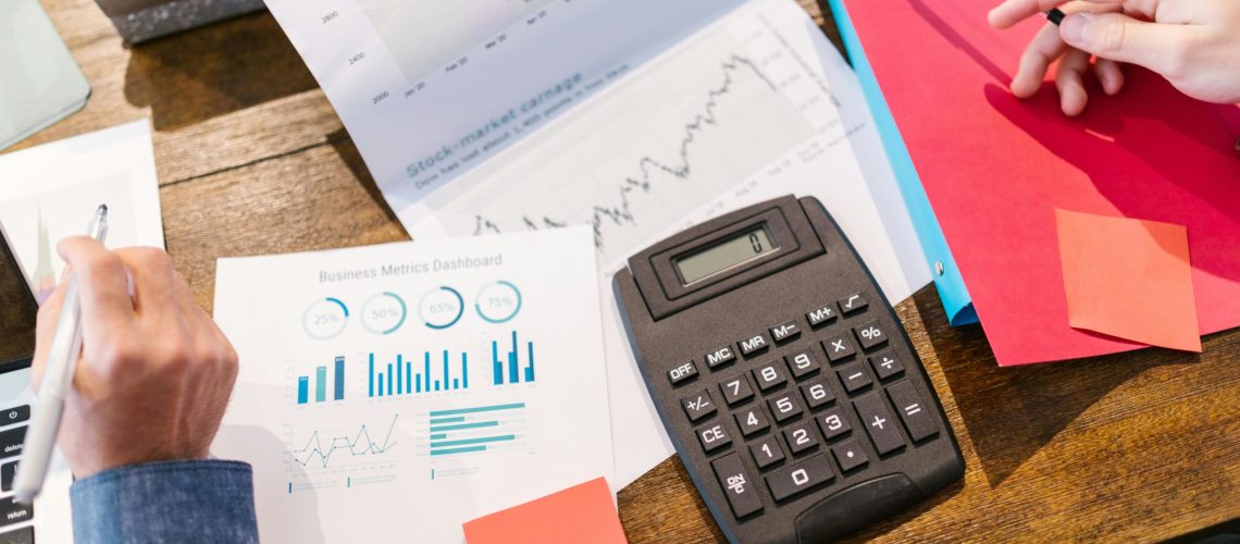 Two professionals analysing financial and marketing performance charts with a calculator and reports on a wooden desk.